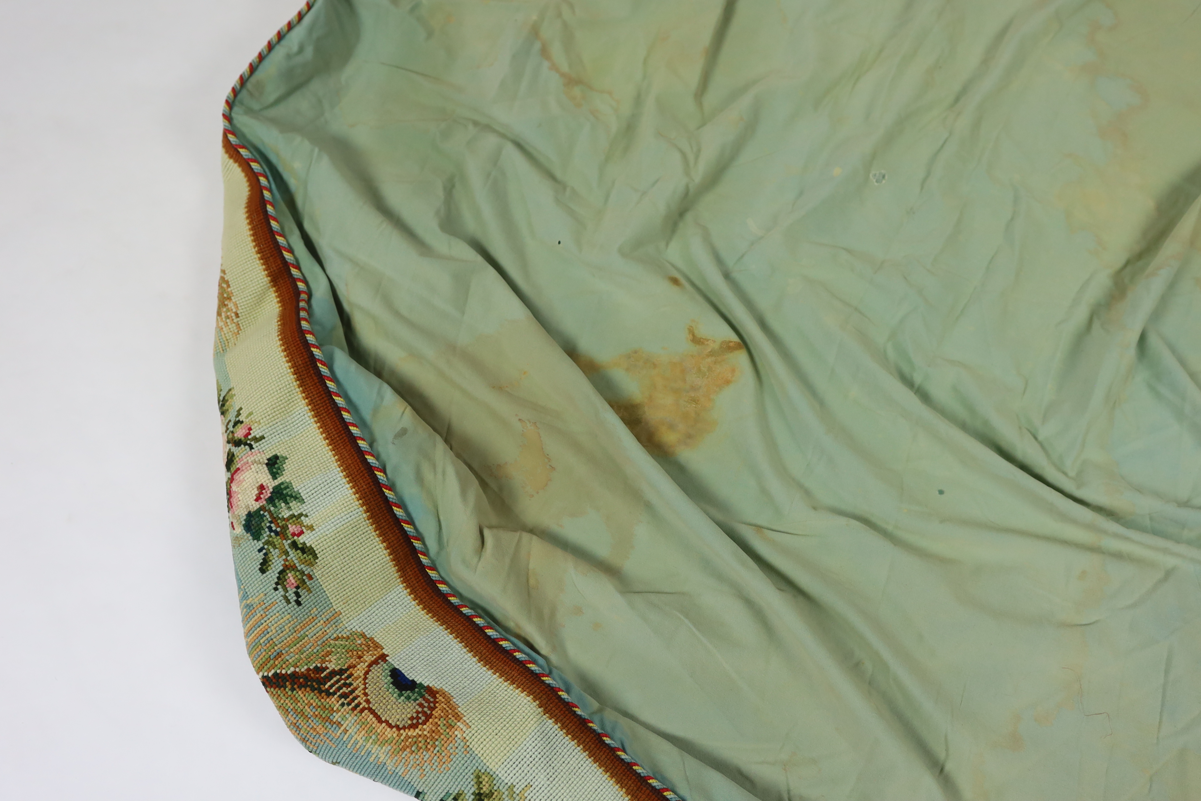 A 19th century Berlin hand wool worked floral and peacock feather designed border, with a deep fringe and cording along the top edge, used as the outer edge/border to a plain cotton turquoise table cover, the wool work a
